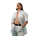 Woman wearing an open white shirt over a patterned top with light-colored pants on a white background