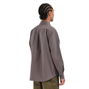A man with braided hair is shown from the back wearing a long-sleeve button-down Last Resort shirt in a muted gray-brown color, paired with olive green pants, against a plain white background.