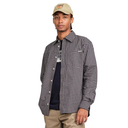 A man wearing a black and white checkered button-down shirt over a dark t-shirt, khaki pants, and a beige baseball cap, photographed against a solid white background.