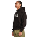 A man wearing a black pullover hoodie with a distressed white graphic on the left chest, paired with olive green pants, shown in profile against a plain white background.