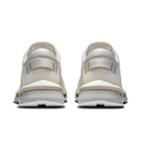 A pair of off-white and beige sneakers shown from the back, featuring a chunky sole and a small debossed brand name on the heel strap.
