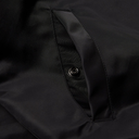 Close-up of a black fabric garment showing a side pocket with a metal snap button closure.