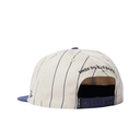 A baseball cap shown from the back, featuring an off-white crown with thin navy pinstripes, a navy blue flat brim, and navy text reading 'TOWNS TO GO HOME' on the back panel.