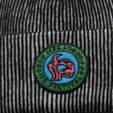 Close-up of a black and white striped knit beanie featuring a circular embroidered patch with a blue background, green border, and pink abstract figure.