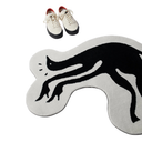 A black cat silhouette-shaped rug in black and white, shown on a white background with a pair of cream low-top sneakers above it.