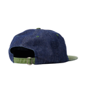 A denim baseball cap shown from the back, featuring a dark blue indigo fabric crown, an olive green adjustable strap with a metal buckle, and an olive green visor.