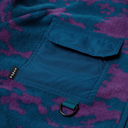 Close-up of a fleece garment with a teal blue and purple camouflage pattern, featuring a flap pocket and a small black brand tag reading 'PUPPY TO'.