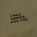 Close-up of olive green fabric with black embroidered text reading 'I WAS GONNA ASK YOU'.