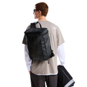 A person shown from the back wearing a black backpack, a beige t-shirt with a white logo, and a white long-sleeve shirt, holding a matching black bag against a plain white background.
