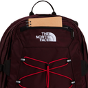 A close-up of a The North Face backpack in dark burgundy, featuring a white embroidered logo on the front pocket, red elastic compression cords, and a brown notebook tucked into the top zipper compartment.