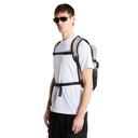 A man wearing a white t-shirt and black cargo pants models a black and gray hydration backpack with a chest strap system against a solid white background.