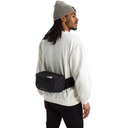 A man wearing a black waist bag from The North Face, styled with a white sweatshirt, black pants, and a gray beanie, shown from a three-quarters back view against a white background.