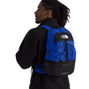 A man wearing a black fleece jacket and black pants, shown from the back and side, wearing a blue and black North Face backpack against a solid white background.