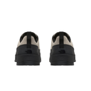 A pair of low-top sneakers shown from the back, featuring a light beige suede upper, black heel panels, and thick black rubber soles, photographed against a solid white background.