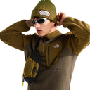 A model wearing a brown and olive green fleece pullover from The North Face, styled with an olive green beanie, white sunglasses, and a matching brown and olive green crossbody bag with yellow piping.