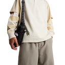 Person wearing a beige sweatshirt and holding a black bag with a visible brand logo on a white background