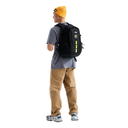 A man wearing a gray t-shirt, tan pants, and a yellow beanie is shown from the back, wearing a black The North Face backpack with bright yellow-green reflective accents.