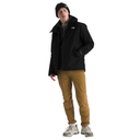A model wearing a black The North Face jacket, black beanie, tan pants, and white sneakers, standing against a solid white background.