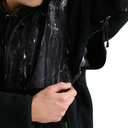 Close-up of a person wearing a black fleece jacket with a glossy black waterproof panel on the chest, showing water beading on the surface and a hand opening a zipper pocket.