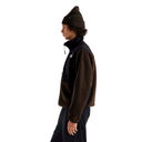 A person shown in side profile wearing a dark brown and black fleece jacket, a matching dark brown beanie, and dark pants against a plain white studio background.