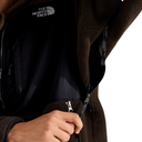 Close-up of a brown fleece jacket with a hand unzipping the front pocket, showing the black interior lining and The North Face logo on the chest.
