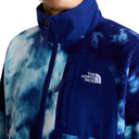 Close-up of a person wearing a fleece jacket with a blue and white tie-dye pattern, featuring a solid dark blue collar and chest pocket with the white The North Face logo.