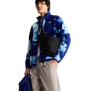 A model wearing a blue and white tie-dye fleece jacket with a black crossbody sling bag, paired with beige cargo pants, against a solid white background.