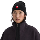 A model wearing a black knit beanie with a red square The North Face logo patch on the front, paired with a dark charcoal fleece zip-up jacket, against a plain white background.