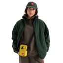 A model wearing a dark green zip-up jacket, olive green hoodie, matching green cap, and a bright yellow crossbody bag with a red The North Face logo, set against a plain white background.