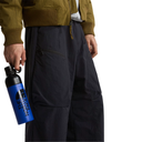 A person wearing wide-leg dark navy pants and an olive green jacket, holding a blue and black The North Face water bottle against a white background.