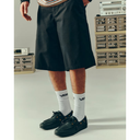 A person wearing black knee-length shorts, white crew socks with a visible Vans logo, and black boat shoes, standing in a studio with vintage audio equipment and crates in the background.