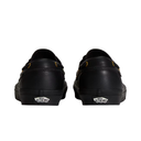 A pair of black Vans slip-on shoes shown from the back, featuring the classic Vans logo on the heel and small yellow accents near the eyelets, set against a plain white background.