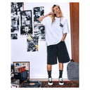 A woman stands in a room wearing a white oversized T-shirt with a small black chest graphic, dark washed denim shorts, black socks, and black-and-white platform sneakers. She is holding a toothbrush to her mouth, with a record player, posters, and a backpack visible in the room.