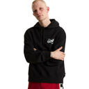 A man wearing a black Vans pullover hoodie with a white graphic logo on the left chest, paired with red pants, photographed against a solid white background