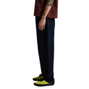 A person shown from the waist down wearing dark navy blue relaxed-fit jeans, a red and green plaid shirt, and bright yellow low-top sneakers against a plain white background.