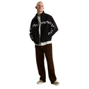 A model wearing a black zip-up jacket with white checkered patterns on the sleeves, a white t-shirt, brown checkered pants, and leopard print sneakers, set against a plain white background.