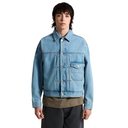A model wearing a light blue denim trucker jacket over a brown shirt and dark gray pants, photographed against a solid white background.