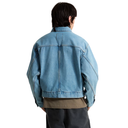 A person shown from the back wearing a light blue denim jacket over a brown shirt and dark pants, photographed against a plain white studio background.