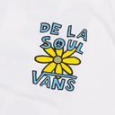 A close-up of a white t-shirt featuring a colorful graphic print with the text 'DE LA SOUL VANS' in light blue and a yellow flower with a peace sign in the center.