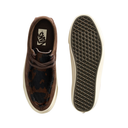 A pair of Vans slip-on shoes shown from the top and bottom on a white background. The shoe features a brown suede upper, a dark brown and black camo-patterned faux fur collar, and a thick off-white rubber sole with a black textured Vans waffle pattern.