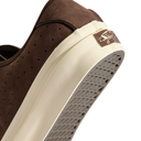 Close-up of a brown suede sneaker showing the side profile, perforated upper, thick cream midsole, and gray waffle outsole. A small brown Vans logo patch is visible on the heel.