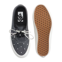 A pair of Vans slip-on shoes shown from the top and side, featuring a dark gray canvas upper with white polka dots, white laces, a black flower detail, and a brown waffle-patterned sole.