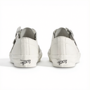 A pair of white Vans slip-on sneakers shown from the back, featuring white rubber soles with black Vans logos and white laces, set against a plain white background.