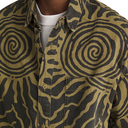 Close-up of a person wearing a button-up shirt with a bold spiral and wavy abstract print in olive green and black, layered over a white crew-neck undershirt.