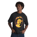 A man wearing a black crewneck t-shirt with a yellow and orange graphic print of a blindfolded figure inside an oval, posed against a solid white background.