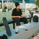 Person sitting on a bench with a skateboard next to them, near a waterfront.