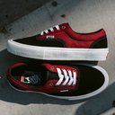 A pair of Vans Old Skool sneakers in black and red canvas with white laces and white rubber soles, photographed outdoors on a concrete surface.