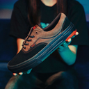 Brown and black sneaker with orange accents held by a person against a dark background