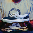 Navy and white sneaker held in front of a person wearing a graphic t-shirt.