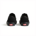 A pair of black low-top Vans sneakers shown from the back, featuring black suede and canvas uppers, black rubber soles, and the signature red Vans logo patch on the heel.